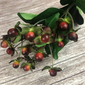 May include: A sprig of artificial berries with dark red fruit and green leaves. The berries have a gradient of colors, transitioning from red to a darker shade. The leaves are a vibrant green, and the stem is a light green.