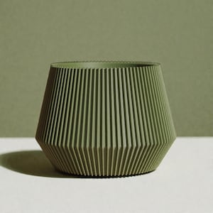 Peut inclure: Un pot vert géométrique avec des détails verticaux en forme de nervures. Le pot a une base large et angulaire qui se rétrécit vers le haut jusqu'à un sommet légèrement plus large. La couleur est un vert olive sourd, et le pot est placé sur un fond vert assorti.