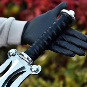 May include: A silver and black sword with a leather-wrapped handle. The sword has a decorative crossguard and pommel. The handle is black and textured. The sword is held by a person wearing black gloves.