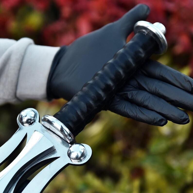 May include: A silver and black sword with a leather-wrapped handle. The sword has a decorative crossguard and pommel. The handle is black and textured. The sword is held by a person wearing black gloves.