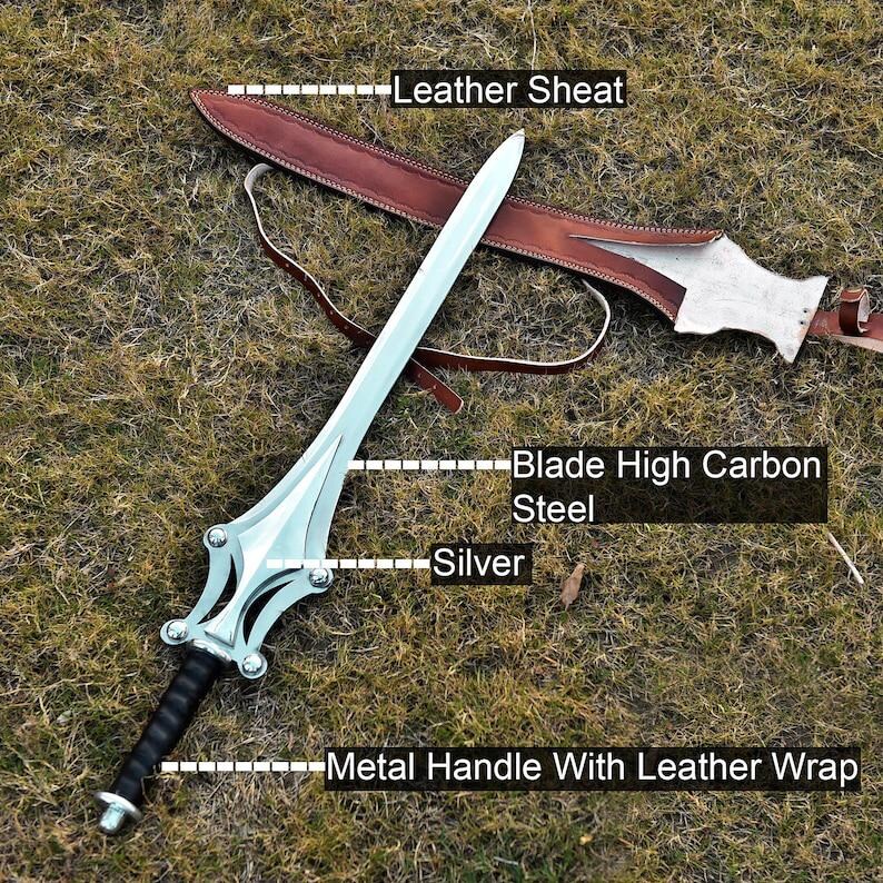 May include: A silver and high carbon steel sword with a black metal handle wrapped in leather, resting on grass. The sword has a decorative silver hilt and is accompanied by a brown leather sheath.