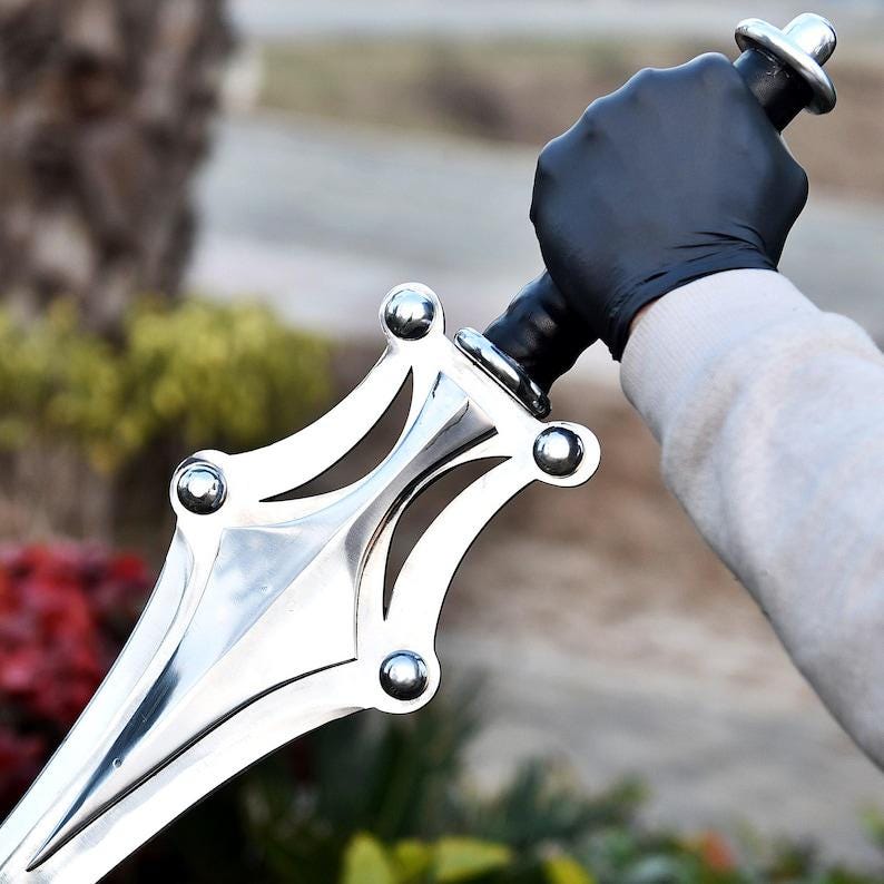 May include: A polished silver sword with a decorative hilt and a black handle. The sword's blade is sharp and pointed. The sword is held by a person wearing a black glove.