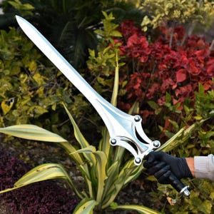 May include: A shiny, silver sword with a decorative hilt and a long, pointed blade. The sword is held against a backdrop of green and red foliage, showcasing its polished metal finish and intricate design.