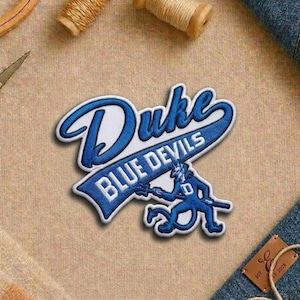 May include: A white ceramic mug with a black handle and the text "But First, Coffee" in a black, handwritten-style font. The mug is on a white surface.