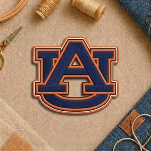 May include: Embroidered patch featuring the letter "A" in navy blue with orange accents. The patch has a white border and is likely a collegiate or team logo. The patch is on a tan fabric surface.