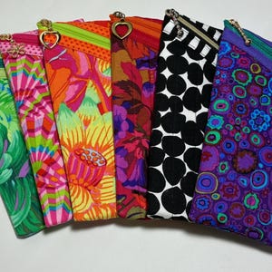 May include: A collection of six quilted fabric cases for spectacles, each featuring a unique colourful pattern including floral, geometric, and polka dot designs. Each case has a diagonal zippered closure with a decorative metal charm pull.