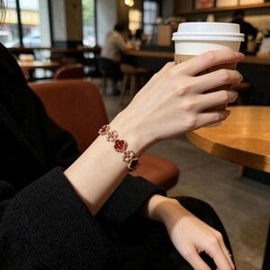 May include: A gold-toned bracelet featuring a series of four-leaf clover-shaped charms with deep red centers, surrounded by small white faux pearls. The bracelet is worn on a wrist, with the metal links connecting each clover motif in a repeating pattern.