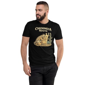 Puede incluir: Camiseta negra con el texto "CHICHIMECA ROOTS" en una fuente estilizada. La camiseta presenta una ilustración detallada de una figura con vestimenta tradicional, arrodillada cerca de una formación rocosa y un cactus. El diseño es en tonos beige, marrón y verde.
