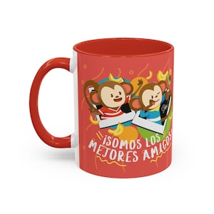 Puede incluir: Una taza de café de cerámica con interior y asa rojos, con un diseño de dos monos de dibujos animados en marcos. La taza tiene el texto "¡SOMOS LOS MEJORES AMIGOS!" en blanco.