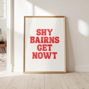 May include: A rectangular wall art print in a thin gold frame featuring the red text SHY BAIRNS GET NOWT centered on a white background. The typography is bold and rounded, presented in four lines of text against the plain white paper surface.