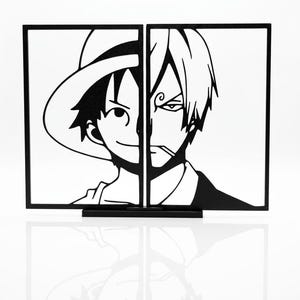 Può includere: Opera d'arte in bianco e nero raffigurante due metà di ritratti di personaggi anime. Un lato mostra un personaggio sorridente con un cappello di paglia, l'altro un personaggio con una sigaretta. La base è nera e il testo "One Piece: A Tale of Two Kings" è in basso.