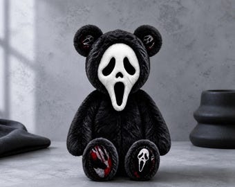 May include: A plush teddy bear with black fur wearing a white Ghostface mask. The bear features round ears with interior patterns, and the soles of its feet display red and black blood-like splatters alongside a small white Ghostface mask icon.
