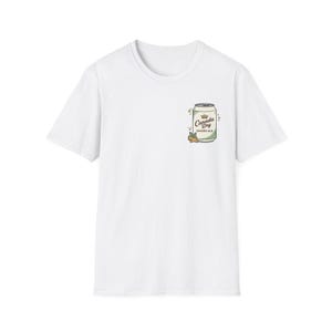 May include: White t-shirt with a small graphic of a Canada Dry Ginger Ale can. The can is light green with the brand name and a crown logo. The design includes a sprig of ginger and a few leaves.