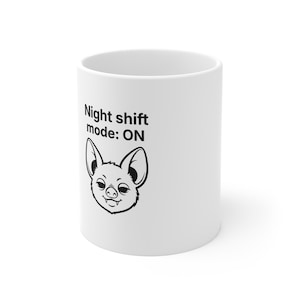 Könnte beinhalten: Weißer Keramikbecher mit dem Text "Night shift mode: ON" und einer schwarz-weißen Illustration einer lächelnden Fledermaus. Der Becher ist zylindrisch und hat eine glänzende Oberfläche.