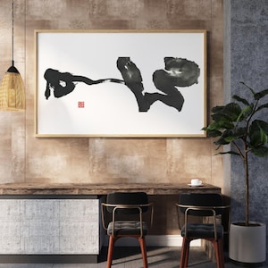 Könnte beinhalten: Ein rechteckiges Wandbild mit schwarzen Tuschepinselstrichen auf weißem Hintergrund, eingefasst in einen hellen Holzrahmen. Das Kunstwerk enthält ein kleines rotes quadratisches Siegel im unteren linken Bereich im abstrakten Kalligrafiestil.