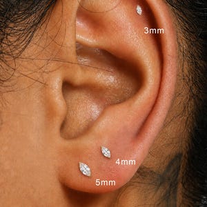 Peut inclure: Gros plan sur une oreille ornée de trois boucles d'oreilles à clous en forme de marquise. Les boucles d'oreilles mesurent 3 mm, 4 mm et 5 mm. L'oreille est claire.