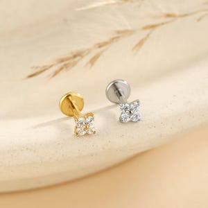 May include: Two flat-back stud earrings, one in gold tone and one in silver tone, each featuring a four-petaled flower design set with clear, sparkling cubic zirconia stones. These small, delicate piercings have a circular base and post.