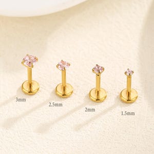 May include: A white ceramic mug with a black handle and the text "But First, Coffee" in a bold, black font. The mug is filled with a dark liquid, likely coffee, and sits on a white surface.