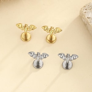 May include: Two pairs of bat-shaped stud earrings with flat back posts. One pair is finished in a polished gold tone, and the other pair is finished in a polished silver tone. Each earring features a detailed bat silhouette with wings spread wide.