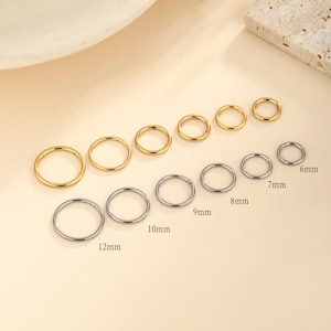 May include: A collection of gold and silver-colored hoop earrings in various sizes, ranging from 6mm to 12mm. The earrings are arranged in rows, showcasing their different diameters. The background is a soft, neutral color.