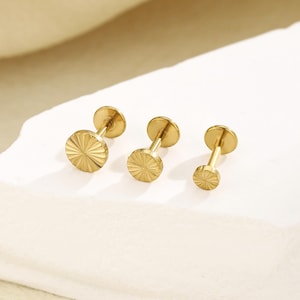 Peut inclure: Trois boucles d'oreilles à clous dorées. Chaque boucle d'oreille présente un motif circulaire texturé sur le devant et une tige. Les boucles d'oreilles sont présentées sur une surface blanche.