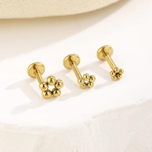 May include: Three gold-toned flat back stud earrings, each featuring a flower-shaped head composed of five small polished spheres arranged in a circular pattern, attached to a straight post with a circular flat base for secure placement.