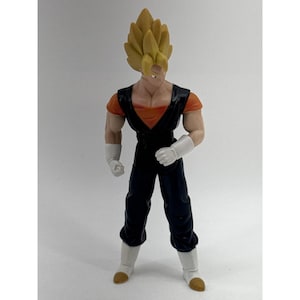 May include: A plastic action figure of a character with spiky yellow hair, wearing a black sleeveless vest over an orange shirt, black pants, white gloves, and white boots with brown tips. The figure stands in a forward-facing pose.