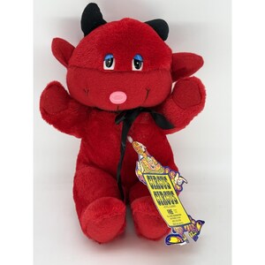 May include: A plush red devil toy with black horns, blue eyes, and a pink nose. It wears a black ribbon around its neck and features a yellow tag with the text Circus Circus Hotel Casino Las Vegas, including a toll-free number and graphic art.