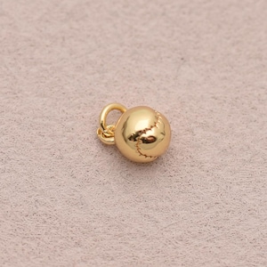 May include: A small, gold-coloured baseball charm with detailed stitching. The charm has a loop for attaching to a necklace or bracelet. The baseball charm is a miniature version of a baseball.