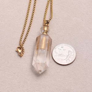 May include: A clear, faceted crystal pendant with a gold-colored metal cap and chain. The pendant is next to a U.S. quarter coin for size comparison. The chain has a lobster clasp.