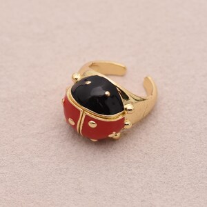 Könnte beinhalten: Verstellbarer Ring in Goldoptik mit einem Marienkäfer-Design. Der Marienkäfer hat einen schwarzen Kopf und einen roten Körper mit schwarzen Punkten. Der Ring besteht aus glänzendem Goldmetall.