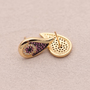 May include: Gold-toned teardrop earrings with a stud backing. The earrings feature a central design of small, sparkling gems in shades of purple, black, and white. The back of the earring has a perforated design.