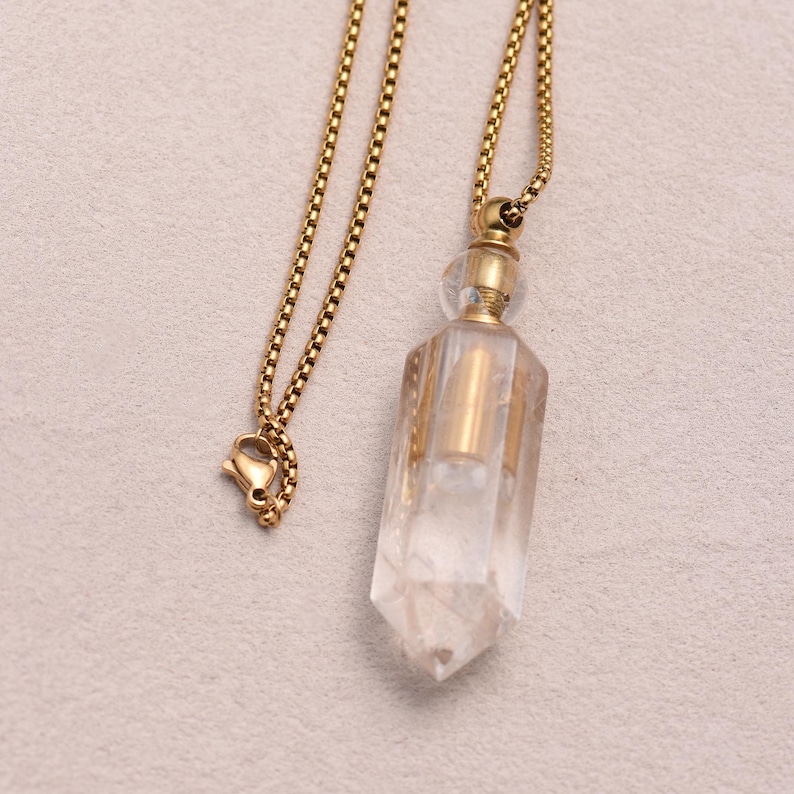 May include: A clear quartz crystal pendant necklace with a gold-colored chain and accents. The crystal is faceted and has a pointed bottom. The chain has a lobster clasp closure.