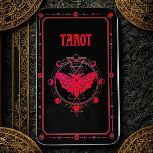 May include: A black tarot card box with a red geometric design and the word "TAROT" in red. The design includes a moth, moons, and geometric shapes. The box is rectangular.