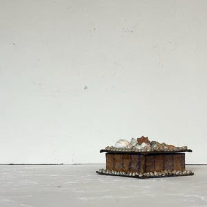 May include: A small, rectangular, brown box with a hinged lid. The box is decorated with small, round, silver-coloured beads around the base and lid. The top of the box is adorned with various seashells.