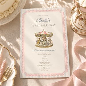 May include: A rectangular first birthday invitation card featuring a pink and blue striped border with lace detailing. The center displays a carousel illustration with the text Amelia's FIRST BIRTHDAY, A little one is turning one!, and event details.