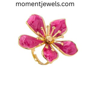 May include: A gold-toned ring featuring a large, stylized flower with five petals. The petals are a vibrant pink with a marbled effect, and the center of the flower is a gold sphere. The ring's band is also gold.