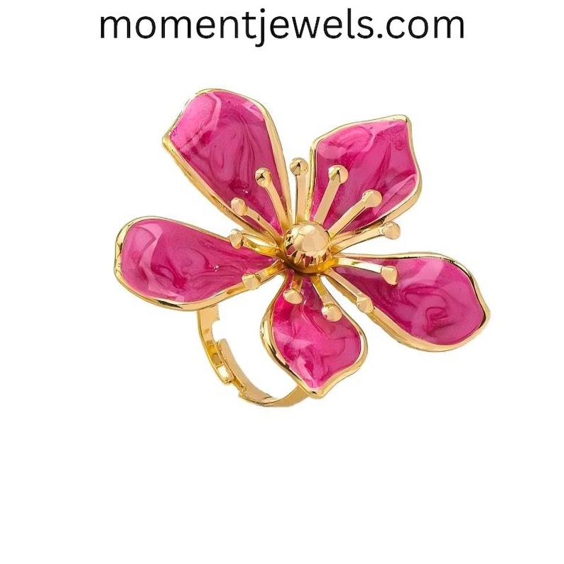 May include: A gold-toned ring featuring a large, stylized flower with five petals. The petals are a vibrant pink with a marbled effect, and the center of the flower is a gold sphere. The ring's band is also gold.
