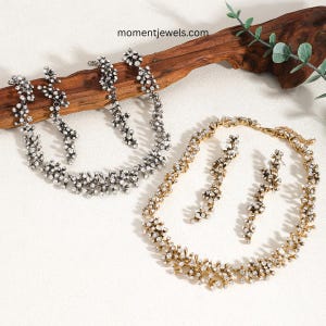 May include: Two jewellery sets, each consisting of a necklace and a pair of earrings, featuring a textured branch-like design encrusted with clear crystals. One set is finished in silver-tone metal, and the other is finished in gold-tone metal.