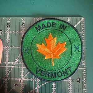 May include: A green and black circular patch with the text "Made in Vermont" and a yellow maple leaf in the centre.