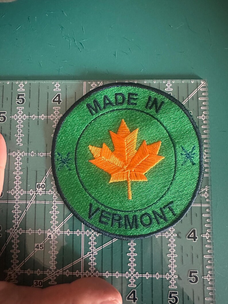 May include: A green and black circular patch with the text "Made in Vermont" and a yellow maple leaf in the centre.