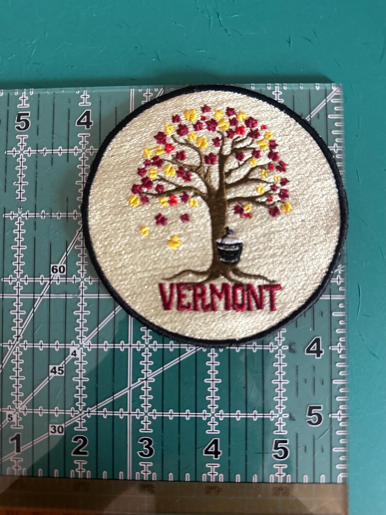 Pode incluir: Patch bordado circular com borda preta e fundo creme. Apresenta uma &aacute;rvore com folhas vermelhas e amarelas e a palavra "VERMONT" em bord&ocirc;. O patch tem aproximadamente 7,6 cm de di&acirc;metro.