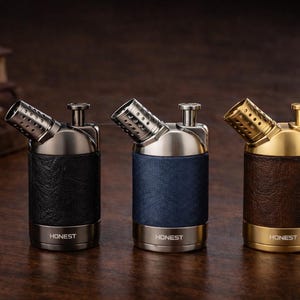 Op de afbeelding: Drie metalen en leren rookpijpen. De pijpen hebben een zilveren, blauwe en gouden afwerking, met leer om de basis gewikkeld. Het woord "HONEST" is op de basis van elke pijp gedrukt.