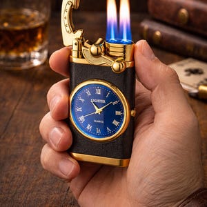 Op de afbeelding: Een goud en zwarte aansteker met een blauwe wijzerplaat. De aansteker is aangestoken en toont twee vlammen. De wijzerplaat heeft Romeinse cijfers en het woord "QUARTZ".