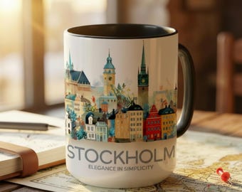 Op de afbeelding: Een witte keramische mok met een zwarte binnenkant en handvat, met een kleurrijke aquarel illustratie van de skyline van Stockholm. Het woord "STOCKHOLM" staat eronder gedrukt, met "ELEGANCE IN SIMPLICITY".