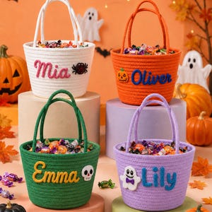 Puede incluir: Cuatro cestas redondas de cuerda en blanco, naranja, verde y morado, cada una con dos asas y llena de dulces variados. Las cestas están personalizadas con los nombres Mia, Oliver, Emma y Lily, acompañadas de pequeños iconos de fieltro.