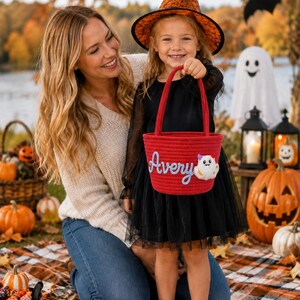 Puede incluir: Una cesta de cuerda roja con asa, que presenta el nombre Avery en letras cursivas azules y una pequeña aplicación de fantasma blanco con detalles en naranja. La cesta está diseñada para recoger objetos y tiene una estructura enrollada.