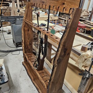 K&ouml;nnte beinhalten: Ein handgefertigter Gewehrst&auml;nder aus Holz mit nat&uuml;rlicher Kante. Der St&auml;nder ist aus dunkelbraunem Holz gefertigt und verf&uuml;gt &uuml;ber mehrere Schlitze zur Aufnahme von Gewehren und Schrotflinten. Der St&auml;nder ist f&uuml;r die Wandmontage konzipiert und hat eine rustikale &Auml;sthetik im Lodge-Stil.