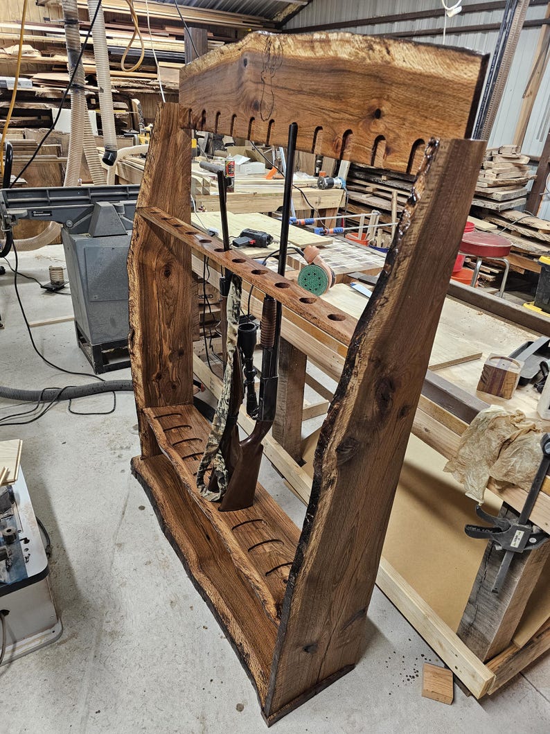 K&ouml;nnte beinhalten: Ein handgefertigter Gewehrst&auml;nder aus Holz mit nat&uuml;rlicher Kante. Der St&auml;nder ist aus dunkelbraunem Holz gefertigt und verf&uuml;gt &uuml;ber mehrere Schlitze zur Aufnahme von Gewehren und Schrotflinten. Der St&auml;nder ist f&uuml;r die Wandmontage konzipiert und hat eine rustikale &Auml;sthetik im Lodge-Stil.