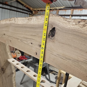 K&ouml;nnte beinhalten: Ein helles, unfertiges Holzbalken mit einer rohen Kante, gemessen mit einem gelben Ma&szlig;band. Das Ma&szlig;band zeigt eine L&auml;nge von etwa 173 cm. Der Balken hat einen Knoten und mehrere L&ouml;cher.